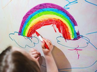 Girl drawing a rainbow with clouds on a whiteboard