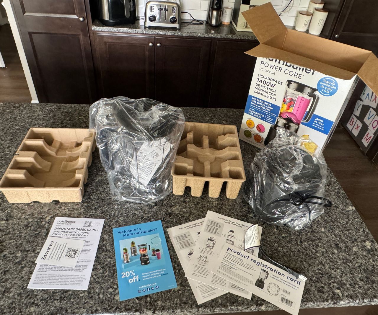 All of the components of the nutribullet PowerCore XL Blender with the instruction manuals beside the box on a stone kitchen counter.