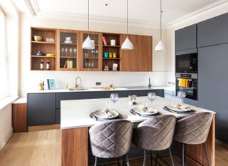 A white kitchen with dark gray and wood cabinetry and wood kitchen flooring.