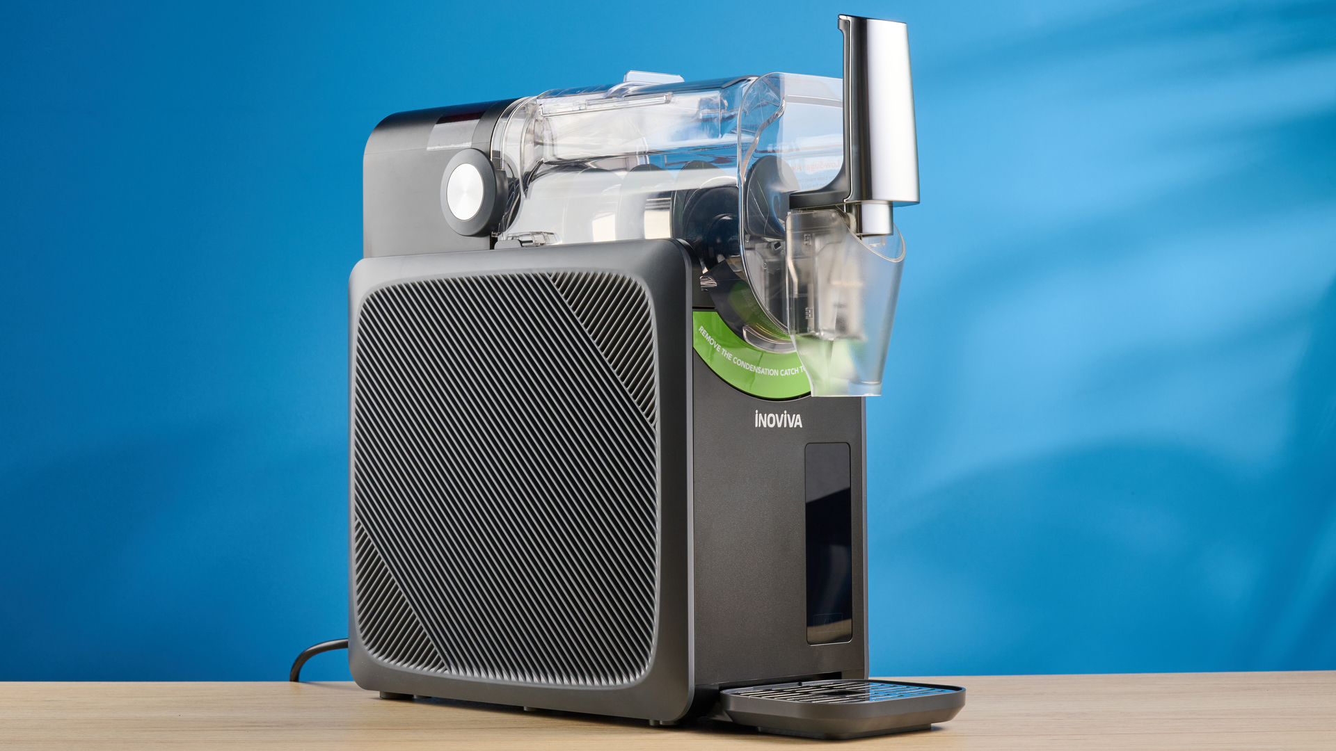 the inoviva slushie machine, a slushie maker with a plastic cylinder body, a dispensing spout, photographed making orange juice slush against a blue tom&#039;s guide background