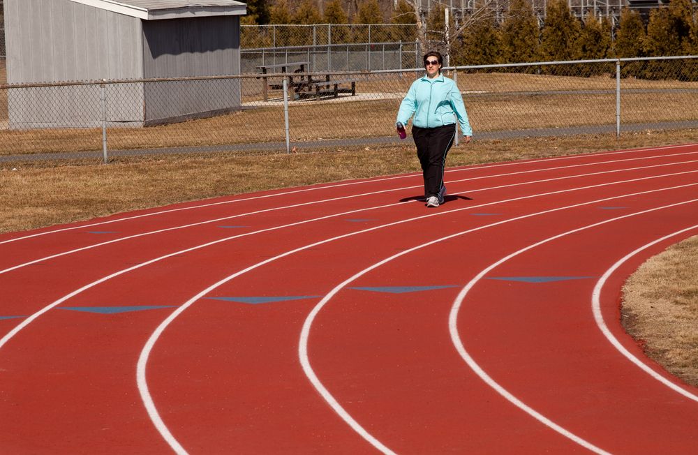 An overweight woman walks around a track.