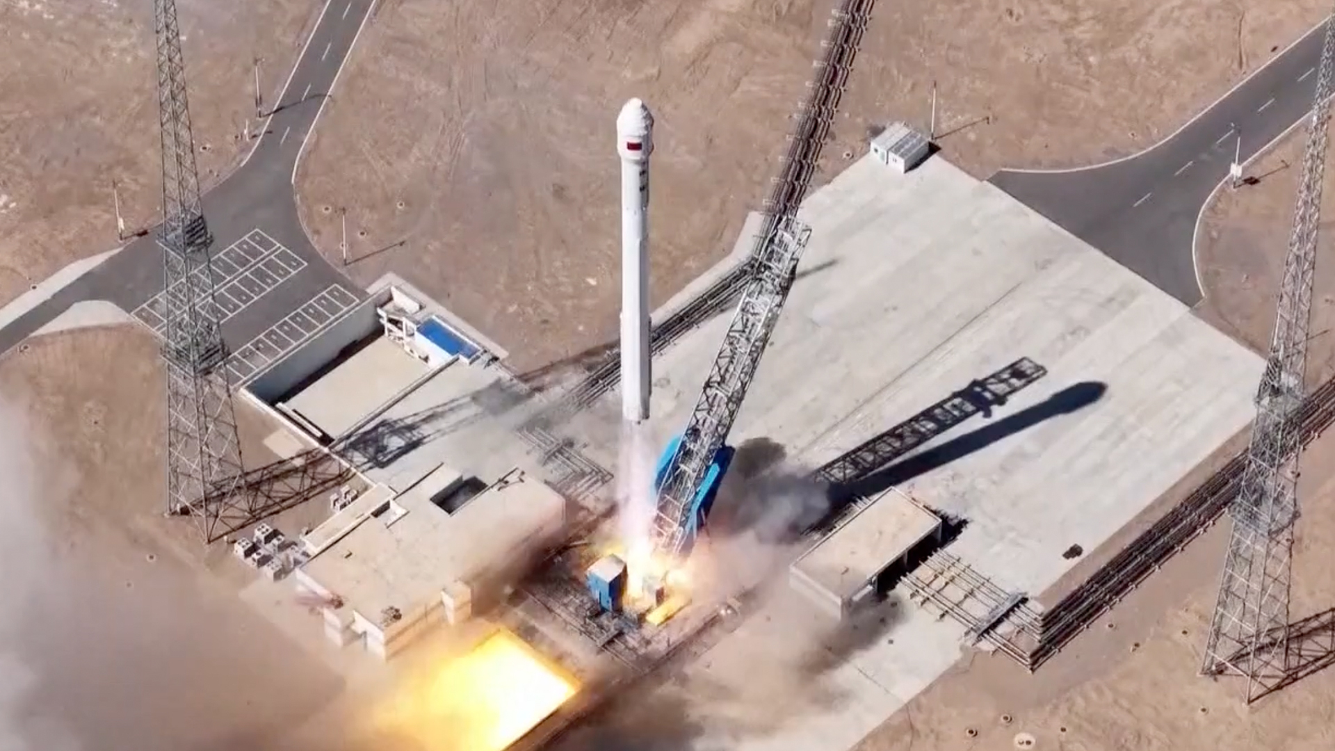 overhead drone photo of a white rocket launching from a desert pad