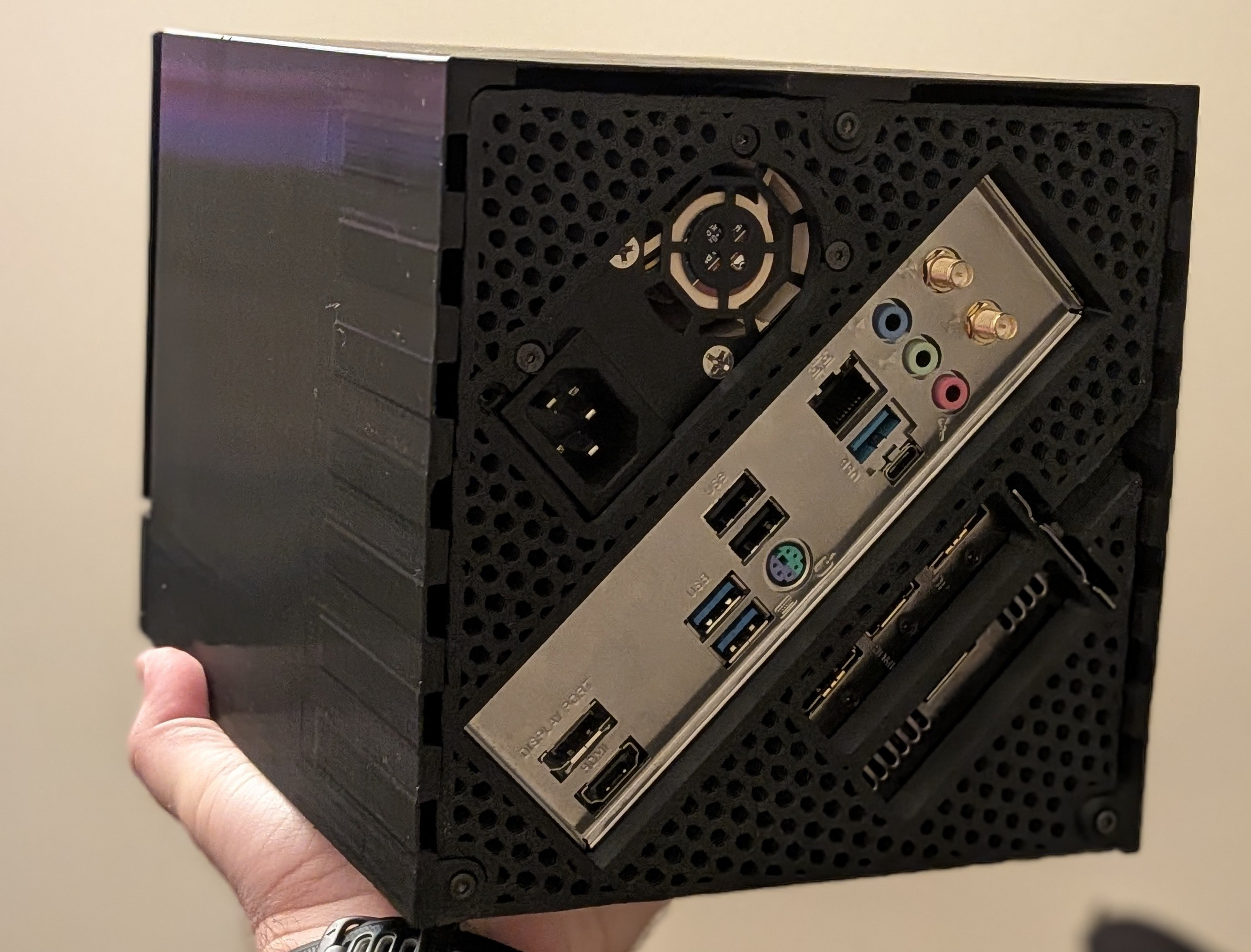 A person holds a compact black computer case, showing various ports including USB, audio, and HDMI connectors on the back panel.
