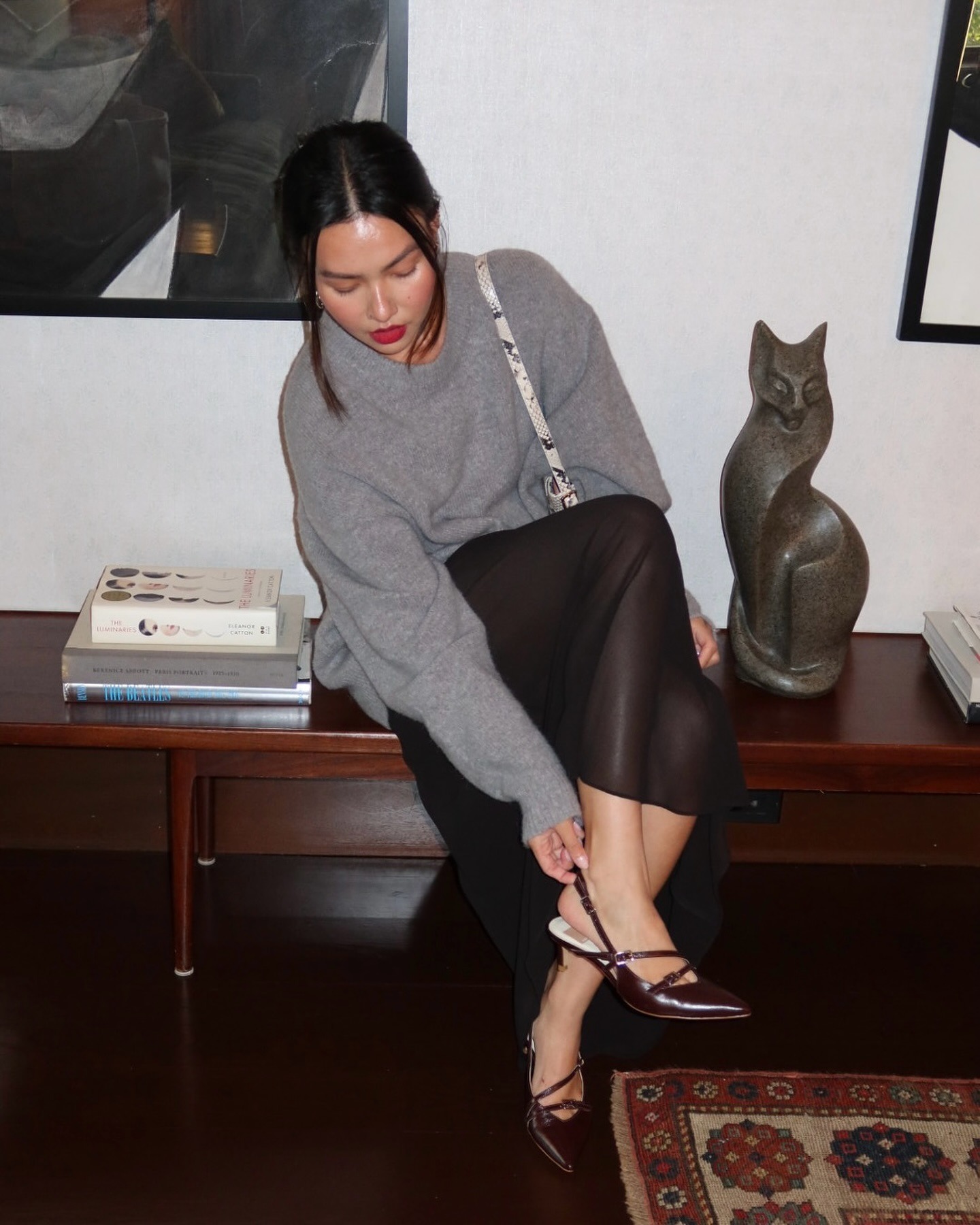 Influencer @mimixn sits on a bend wearing a grey jumper, sheer skirt and brown leather heels.