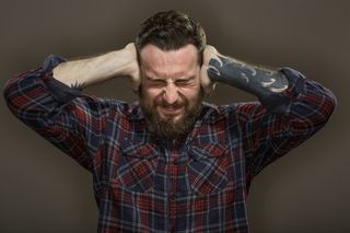 A bearded stressed man covering his ears with his hands.