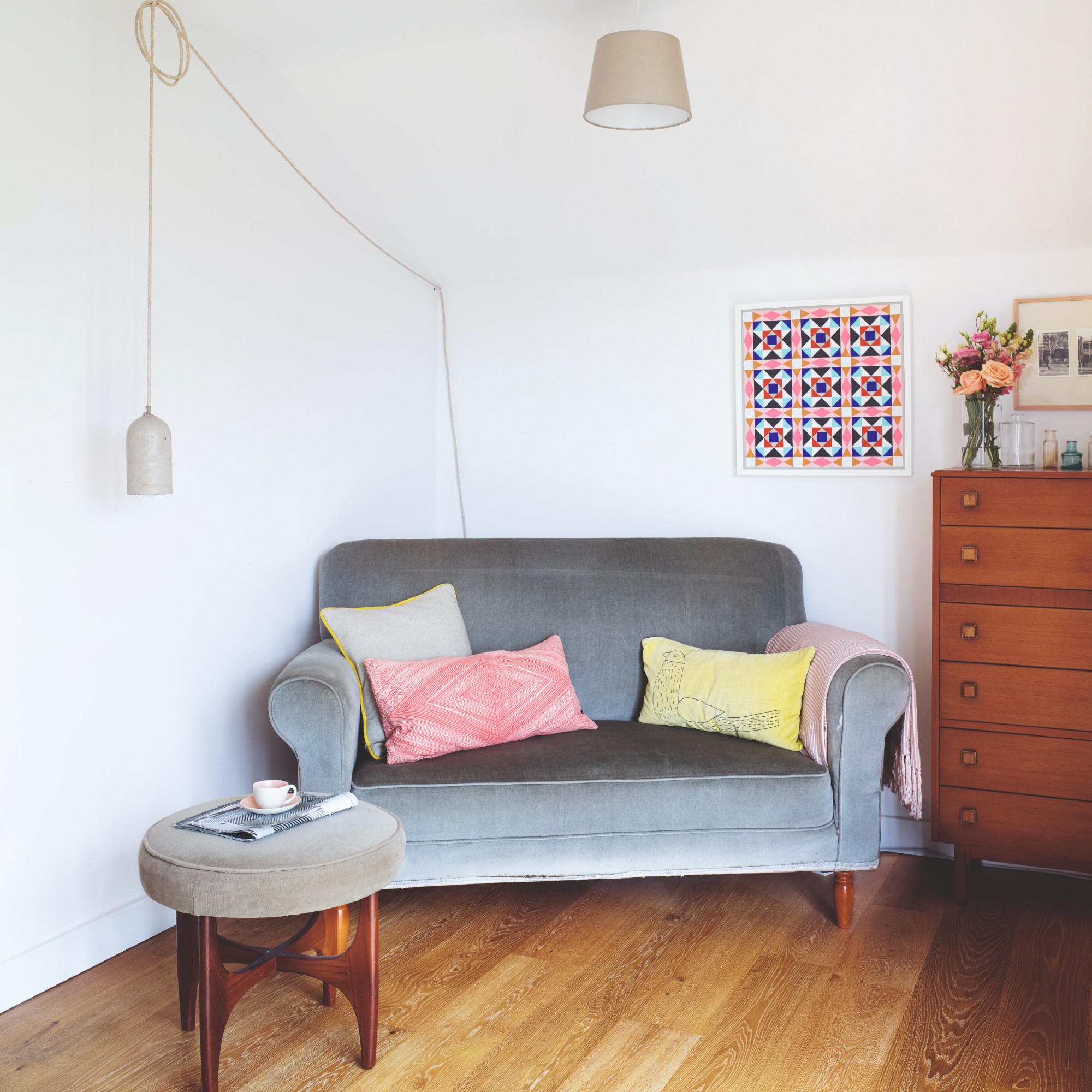 A corner of a room with a grey velvet loveseat and colourful cushions on top