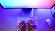 A person using a keyboard in front of a colorful computer monitor