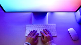 A person using a keyboard in front of a colorful computer monitor