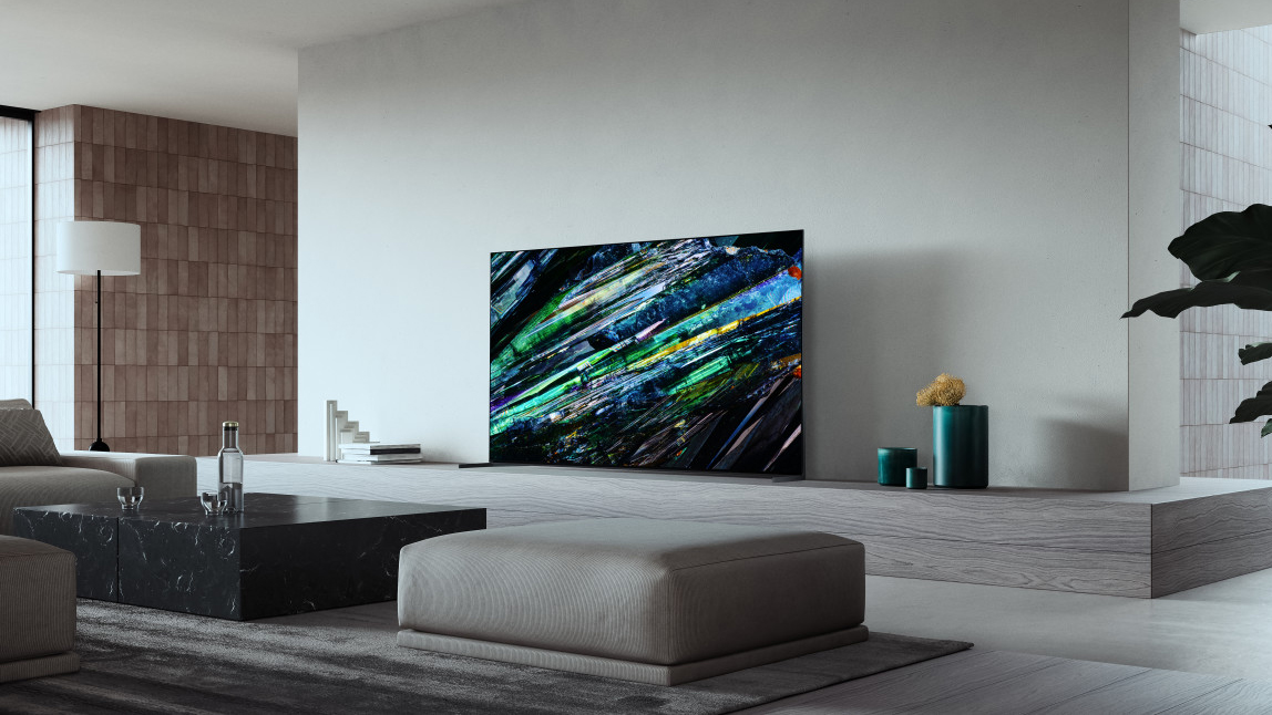 Le téléviseur Sony A95L dans un salon aux couleurs claires, posé sur une étagère