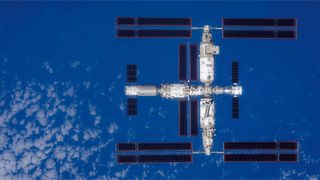 a large T-shaped space station is seen from above with Earth below it