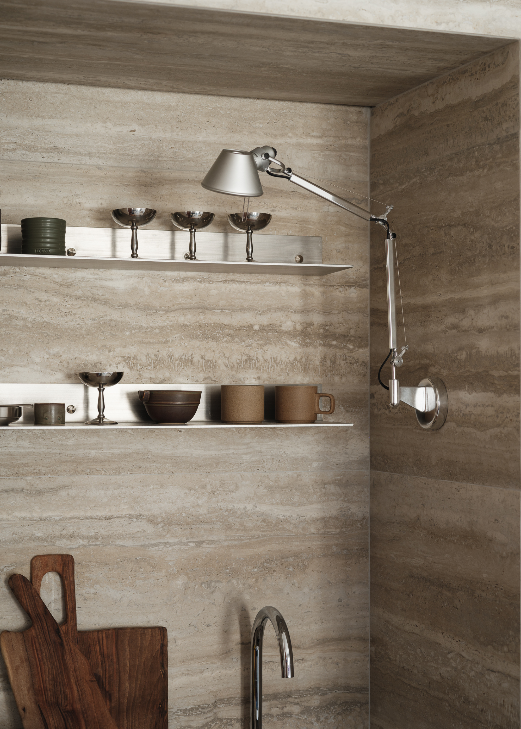 close up of a travertine kitchen with lots of chrome accessories, including a wall light
