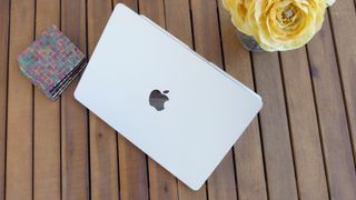 Best MacBook deals, MacBook Air on a wooden table next to a wallat and vase of yellow roses