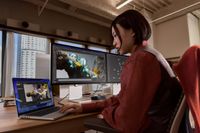 A person works at an office desk on a MacBook Pro connected to two external displays