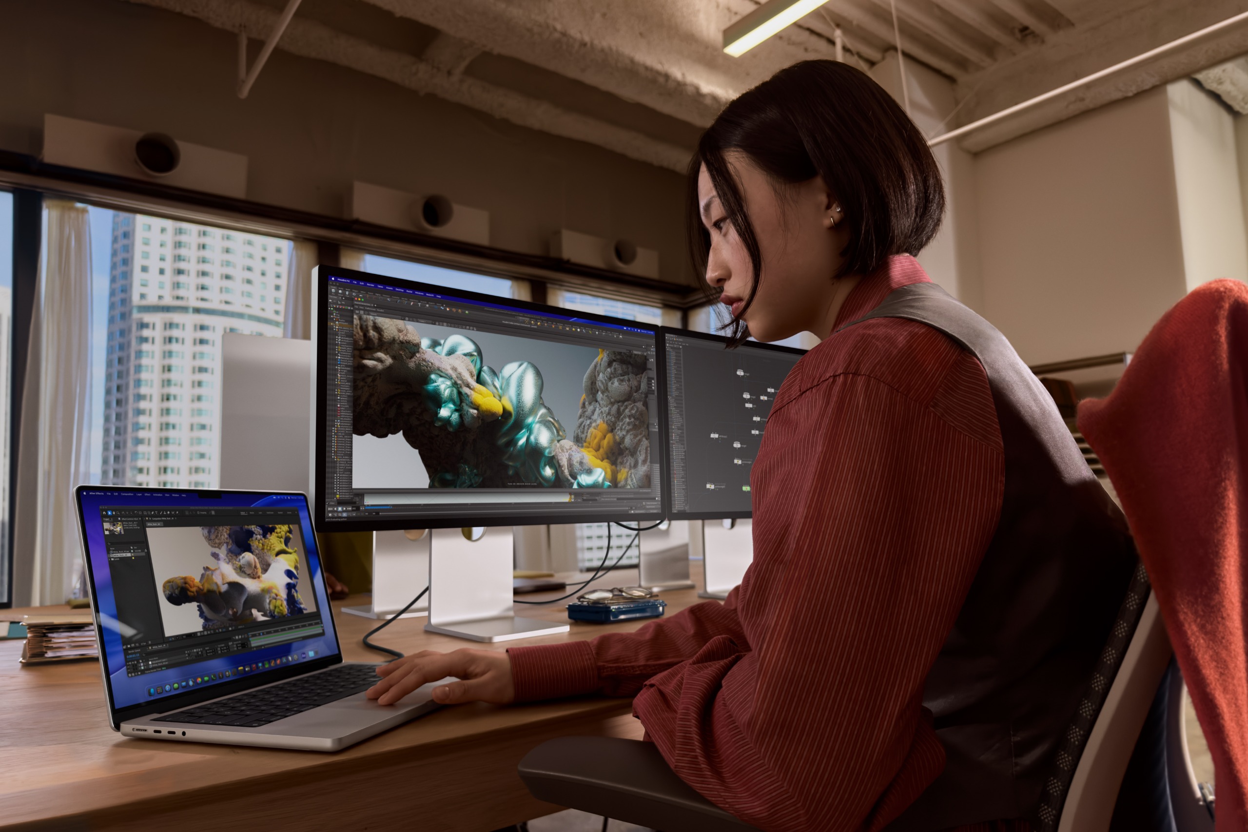 A person works at an office desk on a MacBook Pro connected to two external displays