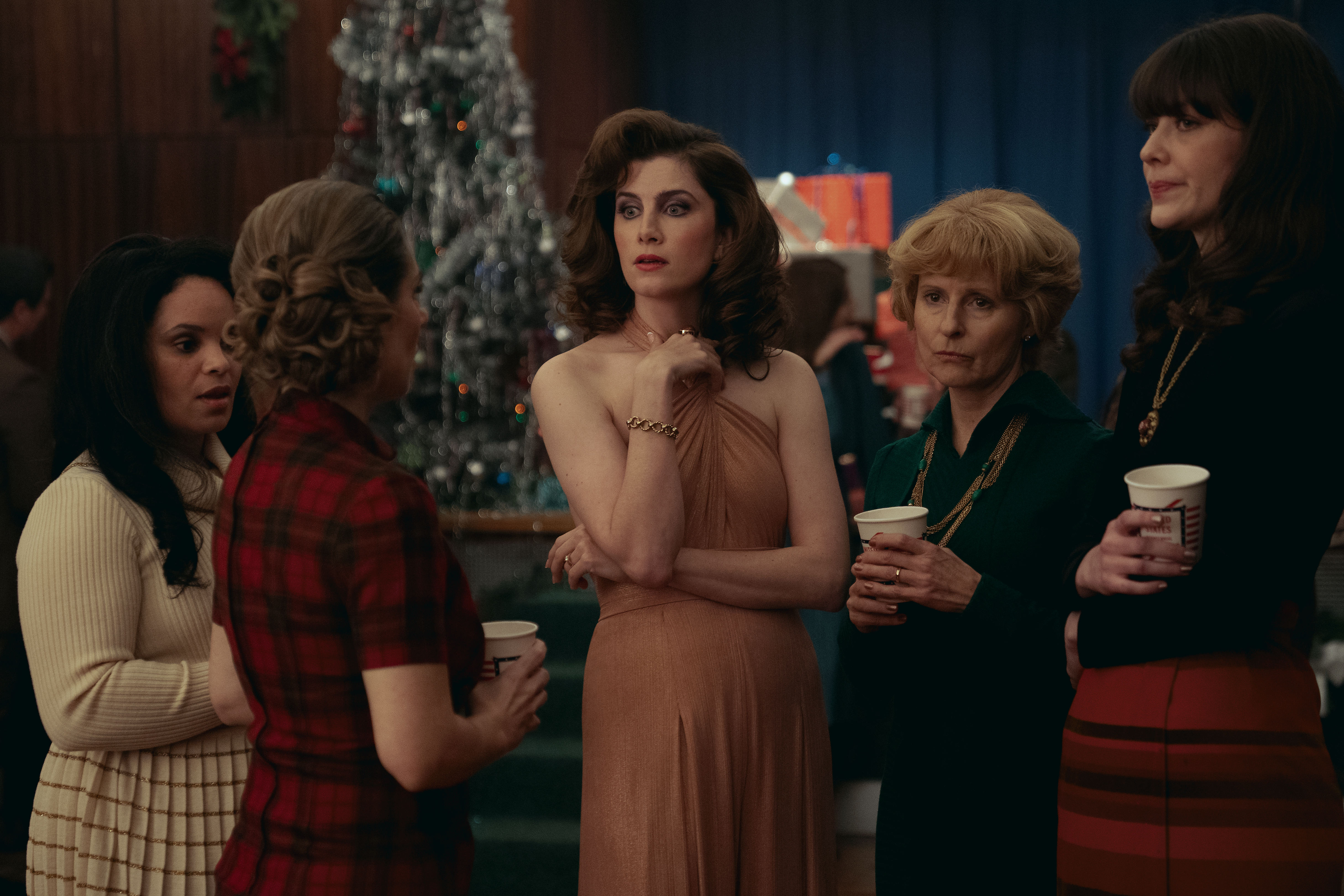 A series of film stills and photographs from a 1970s-inspired set featuring vibrantly decorated interiors with layered furniture and warm lighting, along with characters dressed in vintage clothing whether indoors or at parks, in cards, or at markets outdoors.