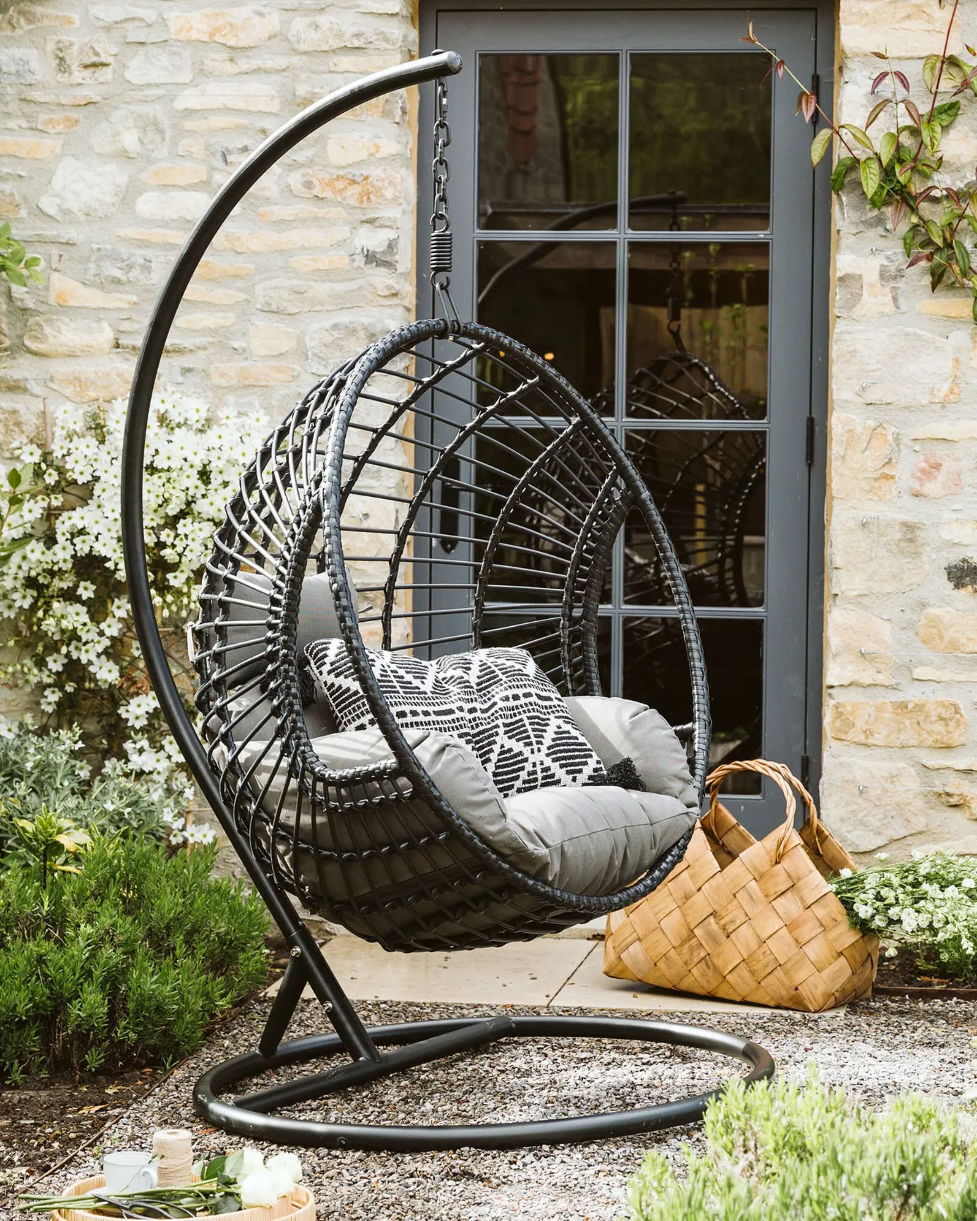 black egg chair with gray cushions on a patio area with green plants