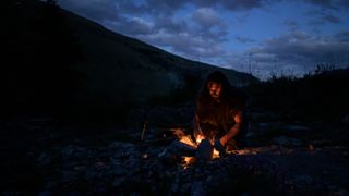 A Neanderthal man crouches around a fire