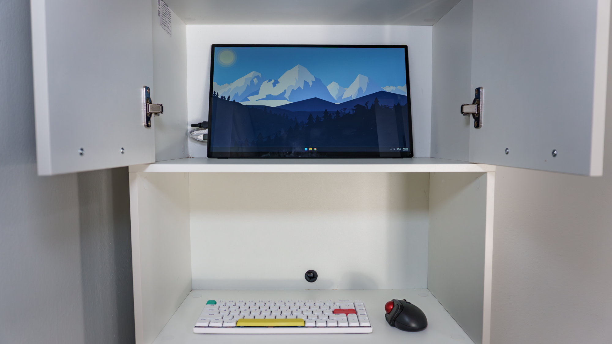 A portable monitor inside a closed compartment of a kitchen pantry cabinet with a mouse and keyboard below it