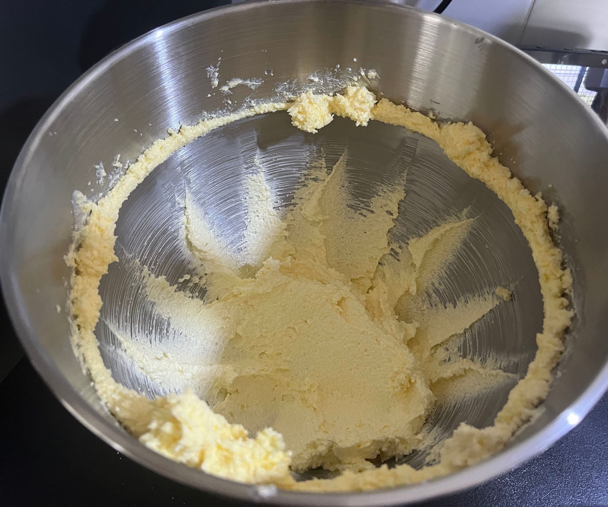 A stainless steel bowl with creamed butter and sugar inside
