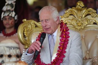 King Charles wears flowers and a gray suit while speaking in Samoa