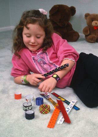 A little girl plays with her "slap wrap bracelets" December 7, 1990 in New York City. The bracelets are made of flexible stainless steel sealed with a fabric or plastic cover. The bracelet can be straightened out, making tension within the springy metal bands. The straightened bracelet is then slapped against the wearer's forearm, causing the bands to spring back into a curve that wraps around the wrist, securing the bracelet to the wearer. (Photo by Yvonne Hemsey/Getty Images)