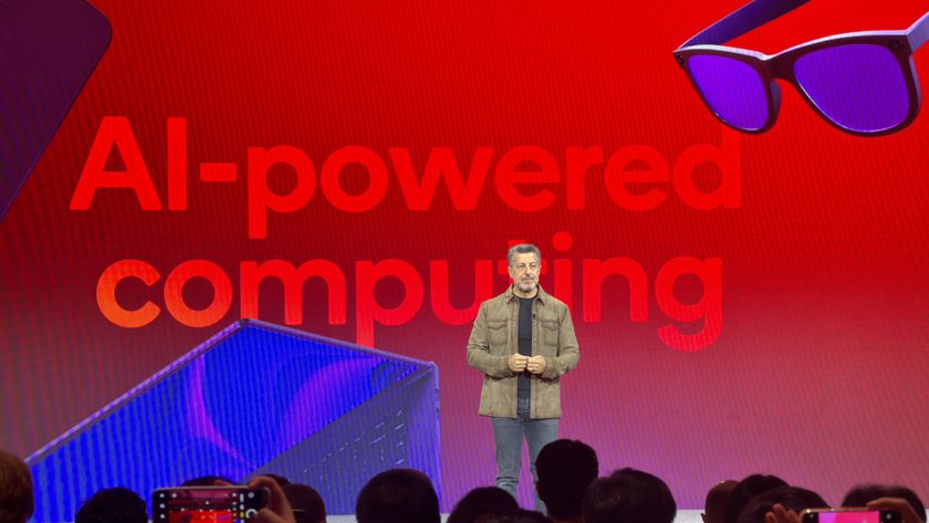 Qualcomm Exec Alex Katouzian in front of a red sign reading &quot;AI-powered computing&quot; with smartglasses floating behind him
