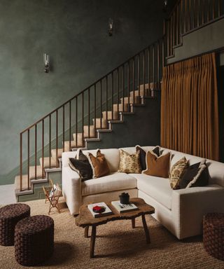 dark green mottled walls in hallway with cream corner sofa and jute rug and brown curtains behind