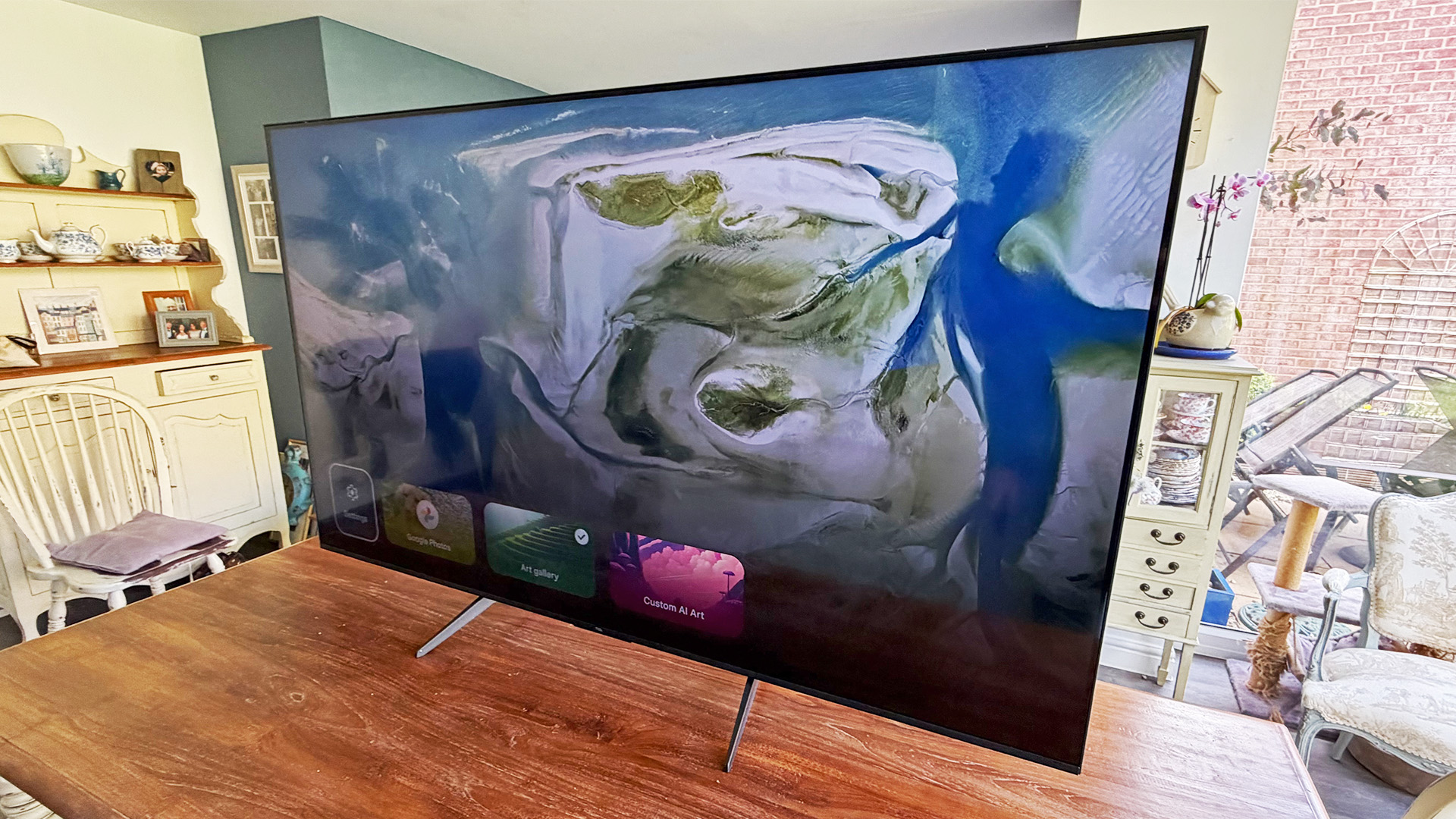TCL Q6C 65-inch LCD TV on wooden dining table, on screen is arial view of geographical features