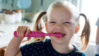 A little girl smiling while brushing her teeth with an electric toothbrush