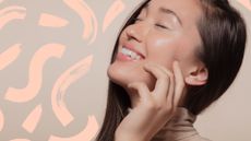 A woman with glowing glass skin smiling and touching her face