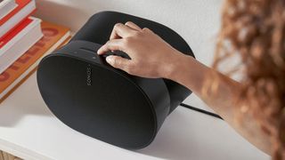 Someone's hand touching the top of a Sonos Era 300 speaker that's sitting on a white surface.