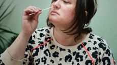 white woman wearing white sweater with colorful animal print tilts her head back in order to insert a long swab into her nose.