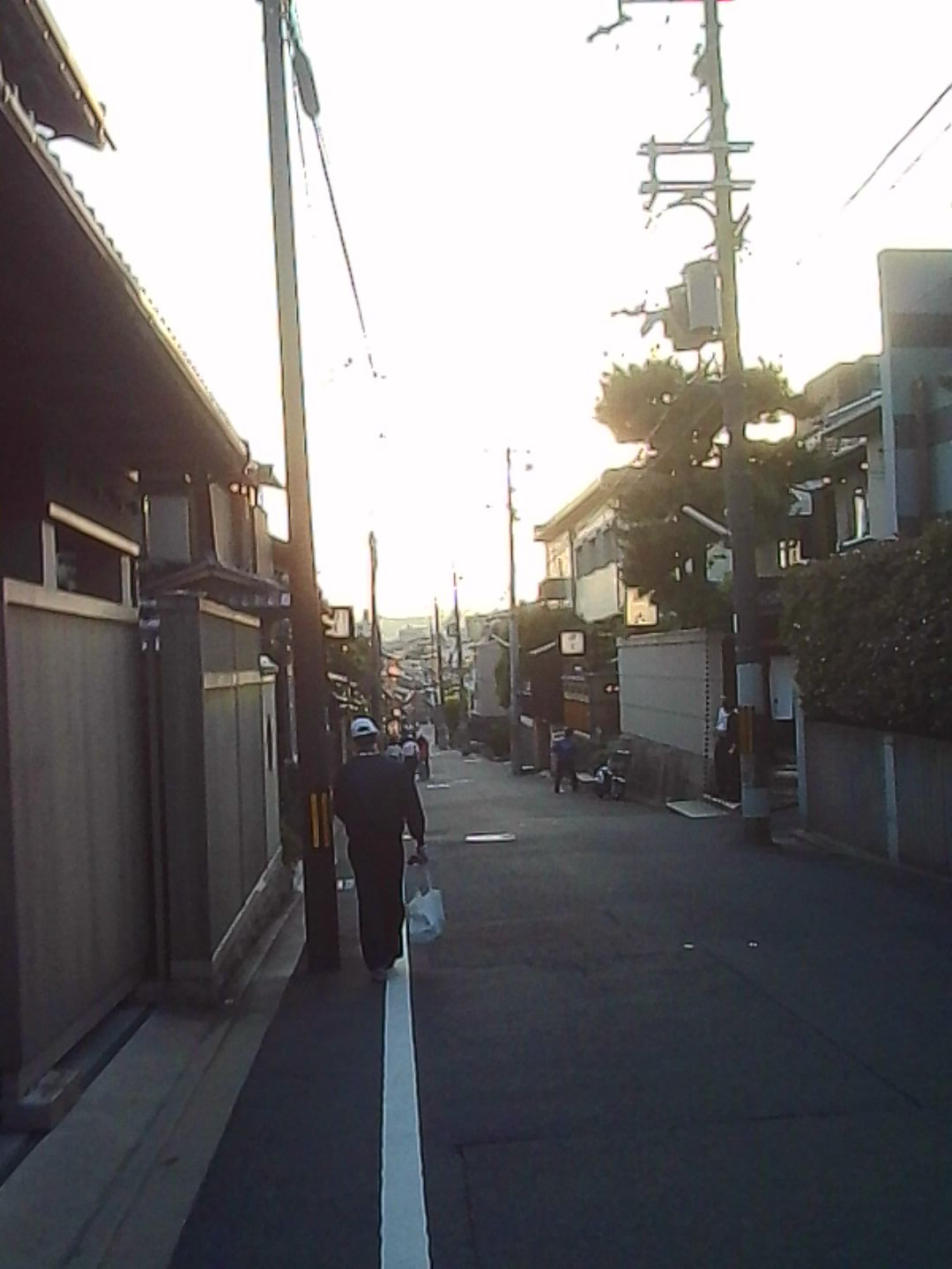 Backlit Japanese street at sunset with pedestrians walking between traditional buildings.