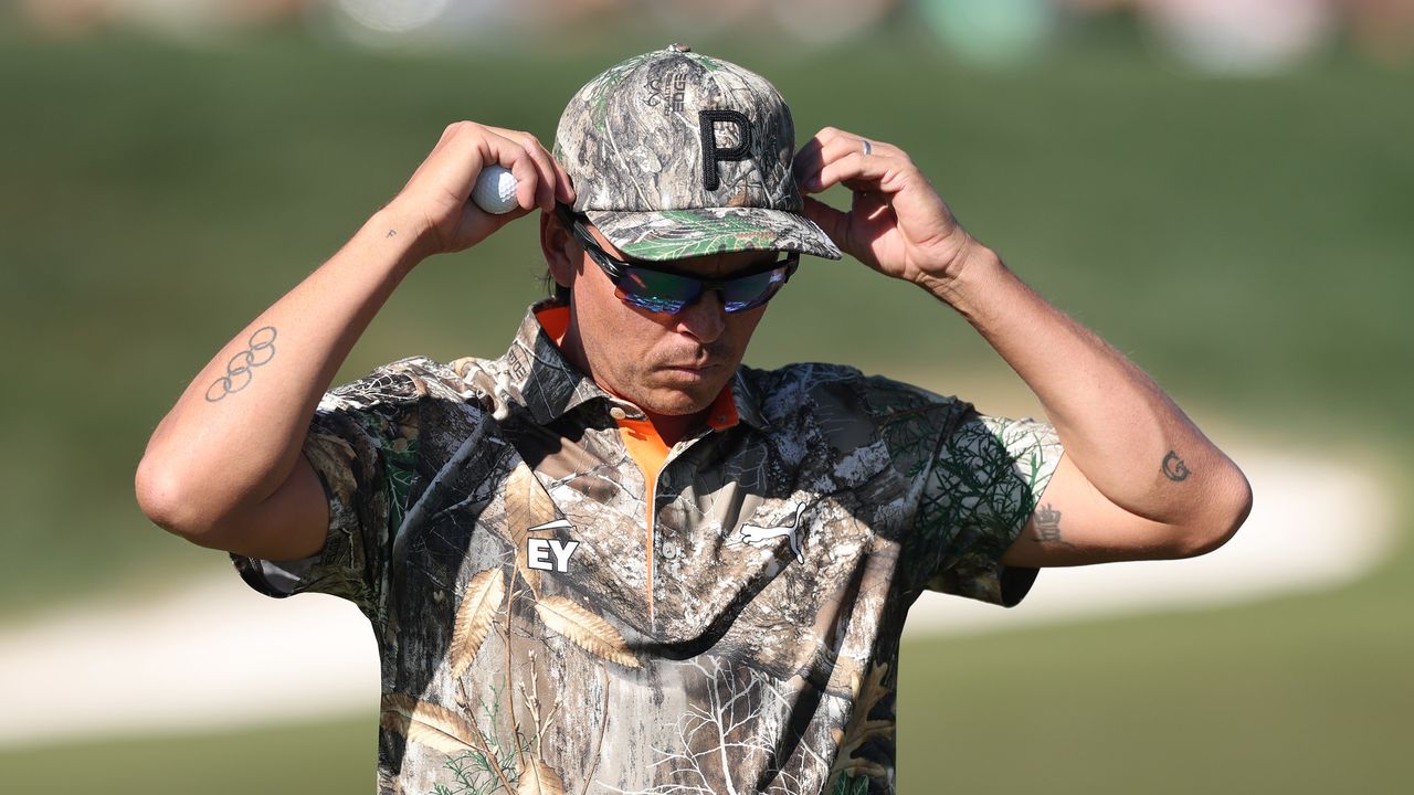 Rickie Fowler wears a camo polo and cap while adjusting his sunglasses at the 2025 WM Phoenix Open