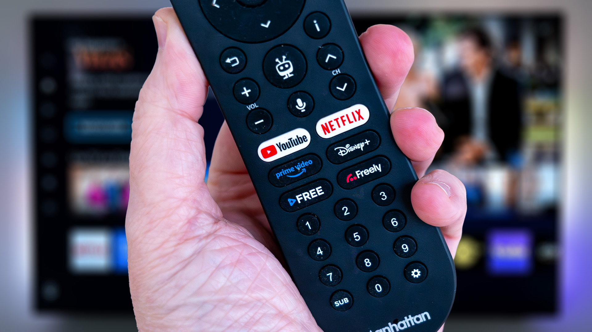 Freely remote control (Manhattan Aero TV) held in hand with Freely on TV in background