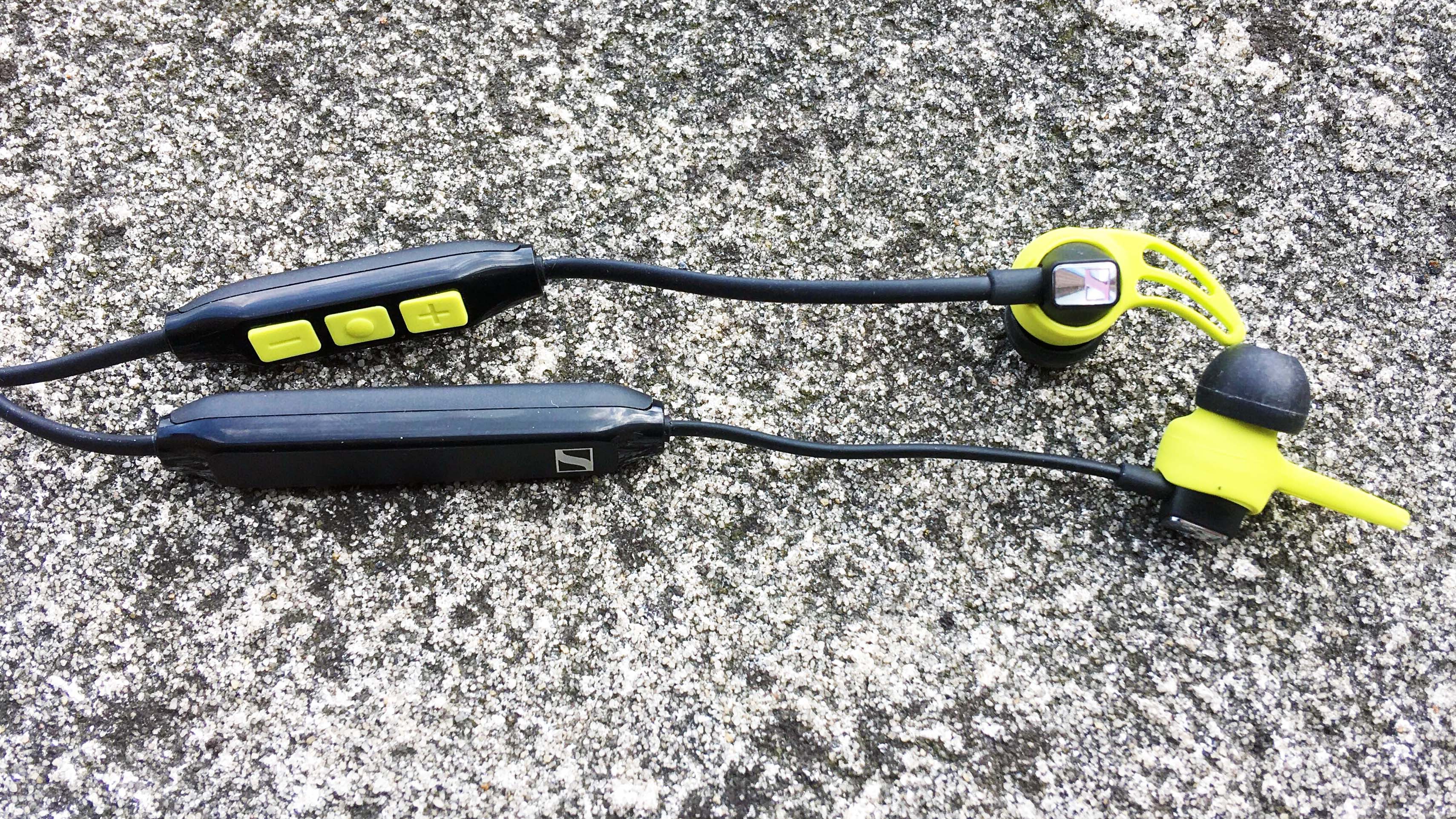 Et par sorte og gule Sennheiser CX Sport ligger på asfalt.