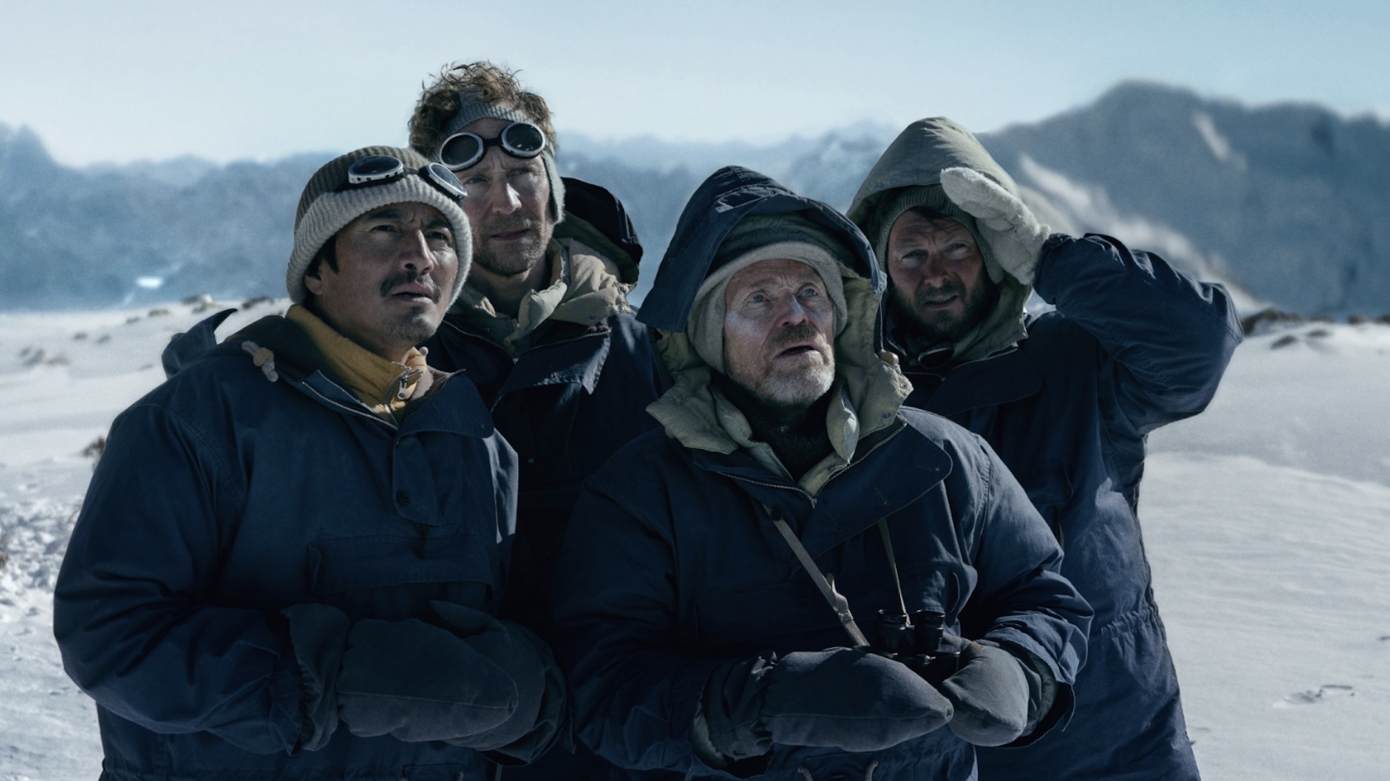 Willem Dafoe, Tom Hidleston,and a group of climbers bundled up in Tenzing on to of a mountain.