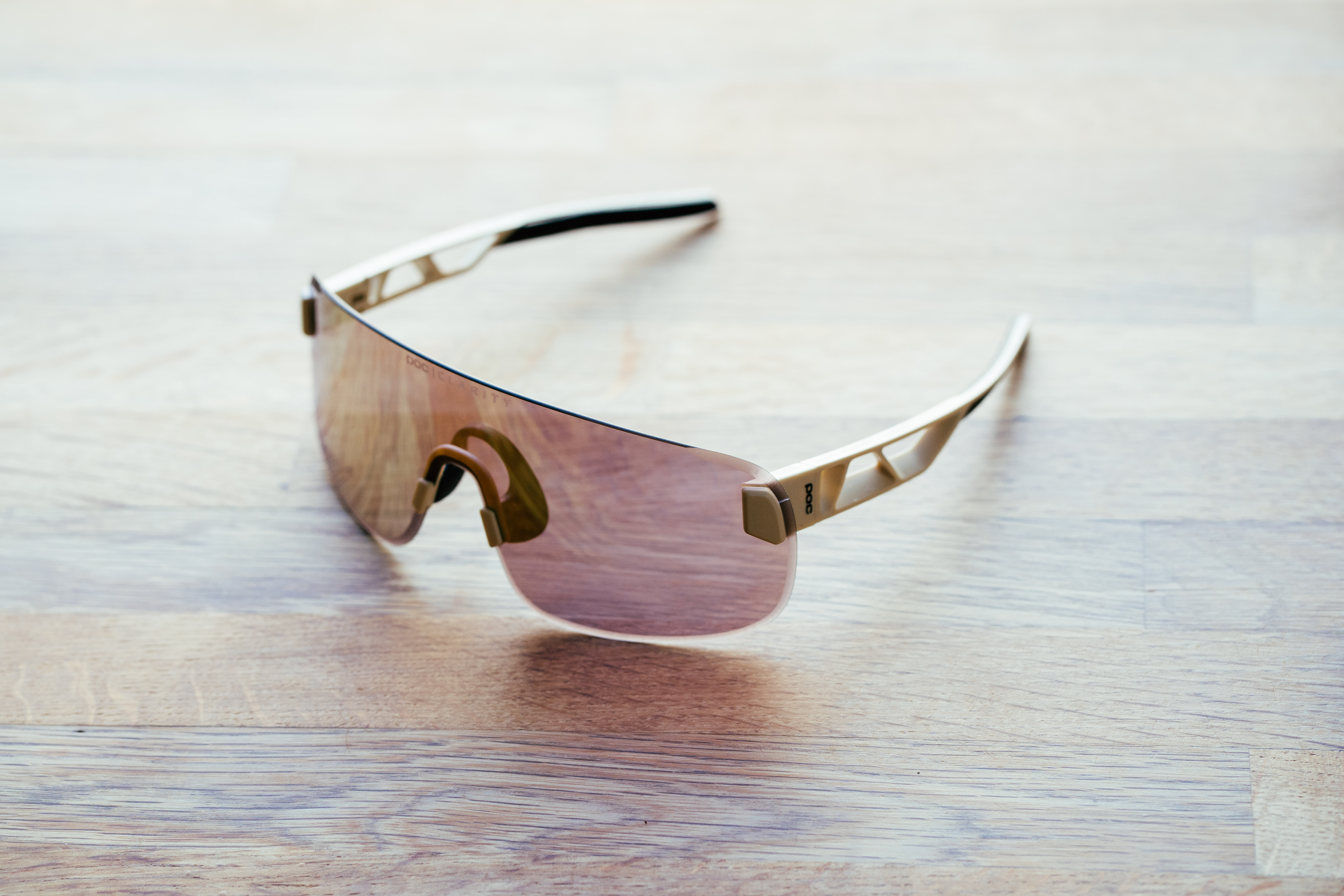 A set of frameless sunglasses with beige arms on a wooden surface