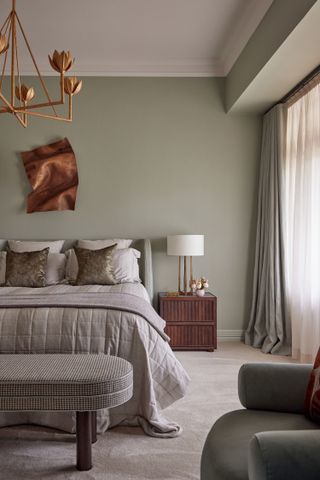 A bedroom with sage green walls, and a metallic wall art and chandelier