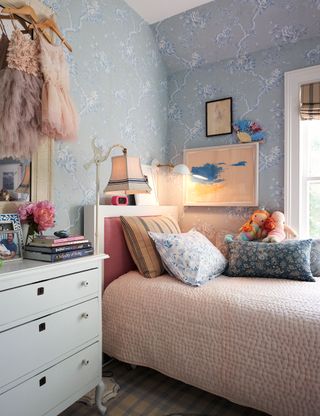 bedroom with pale blue floral wallpaper and pink linen and accessories