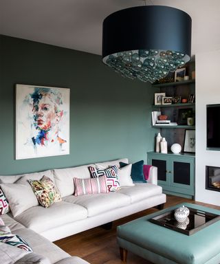 A beige sofa, green wall and fabric and glass pendant light demonstrating small living room lighting ideas.