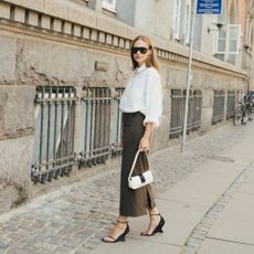 Woman wears white button down, pencil skirt, white handbag, and black wedge heels while posing in the streets of Copenhagen. 