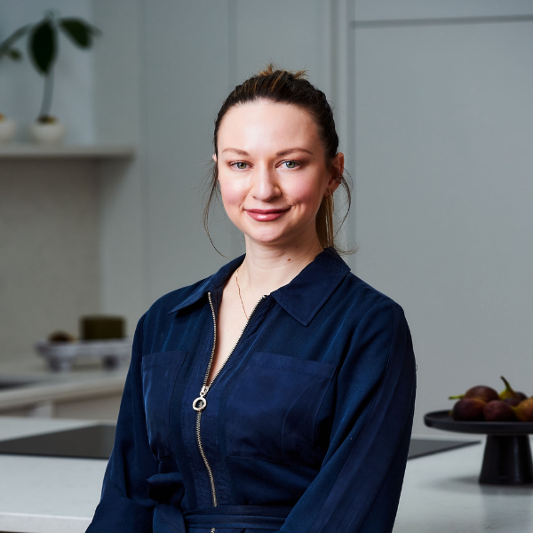 A headshot of Katerina Tchevytchalova, a lady with her brown hair tied back smiling at the camera wearing a navy blue jumpsuit with a zip down the front