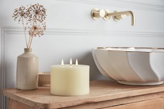 A bathroom vanity with a countertop basin and a three wick candle next to it