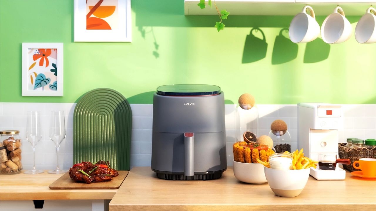 A Cosori LITE air fryer on kitchen countertop with green wall decor