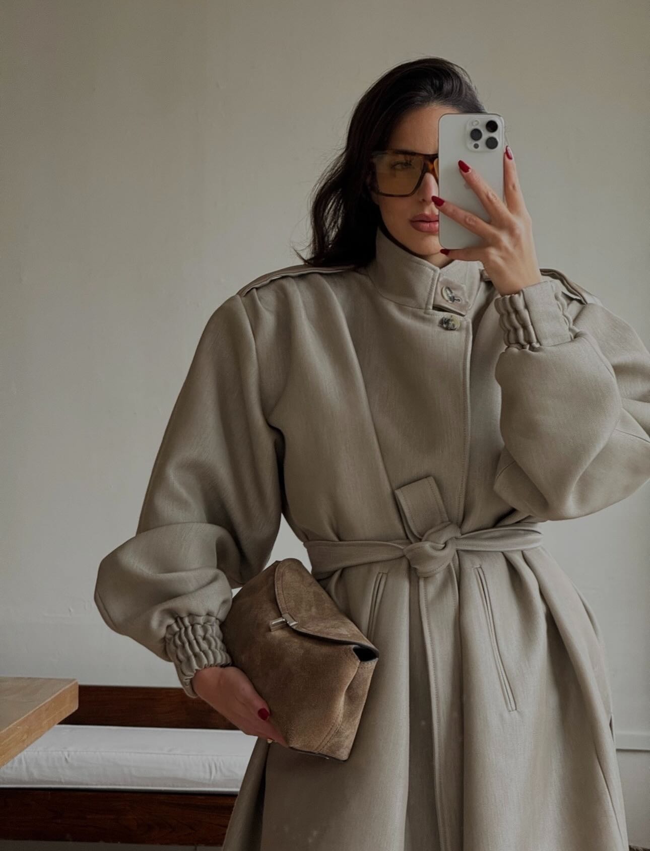 @bettinalooney taking a mirror selfie, wearing a beige tie belt coat