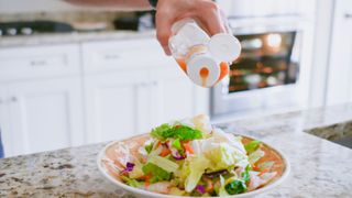 Hand pouring salad dressing over salad on kitchen countertop