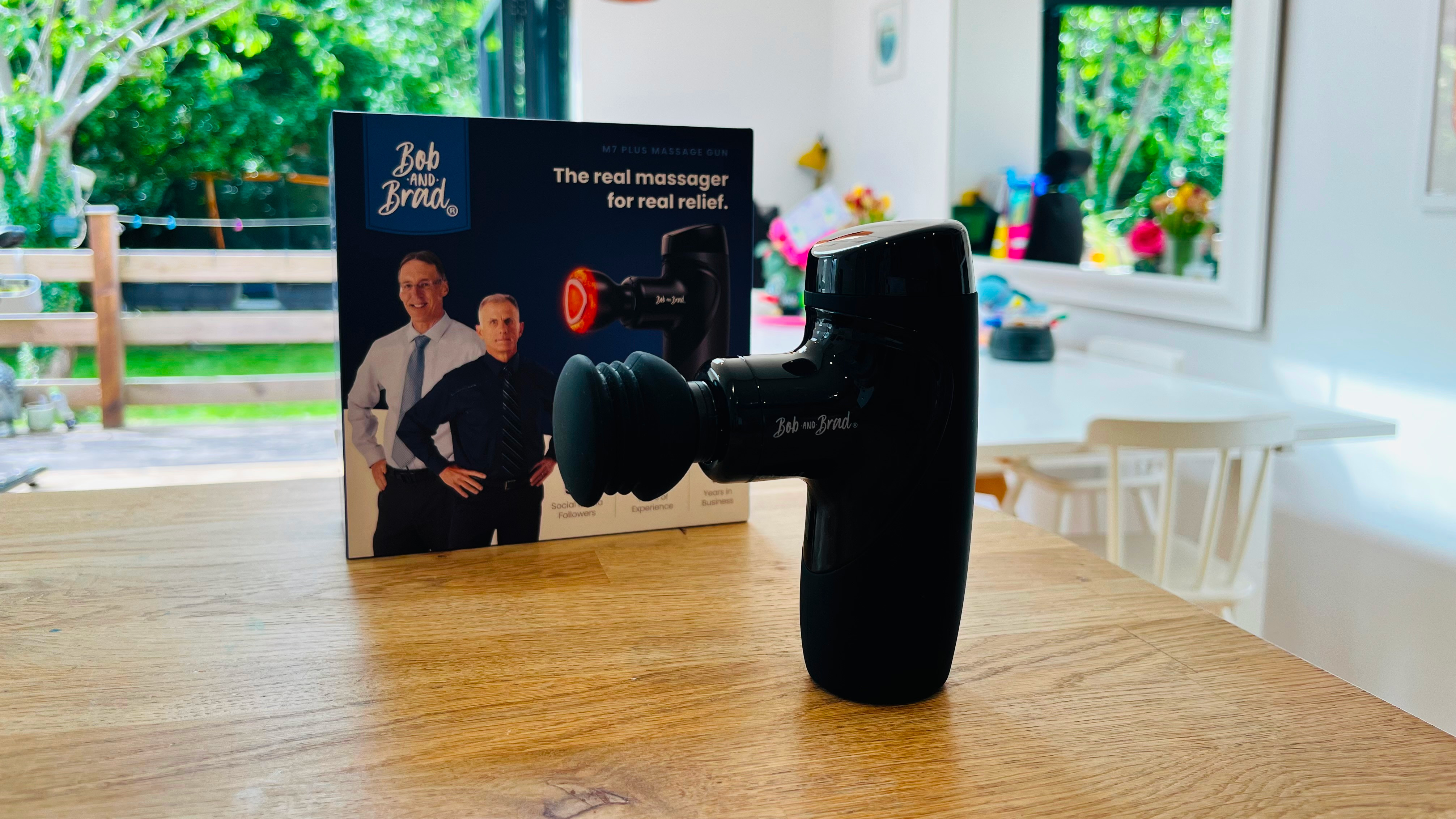Massage gun stands on table in front of box with two men on it and the text "Bob and Brad"