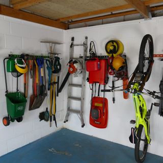 Corner of garage with racks with garden tools, ladder, mower and bike