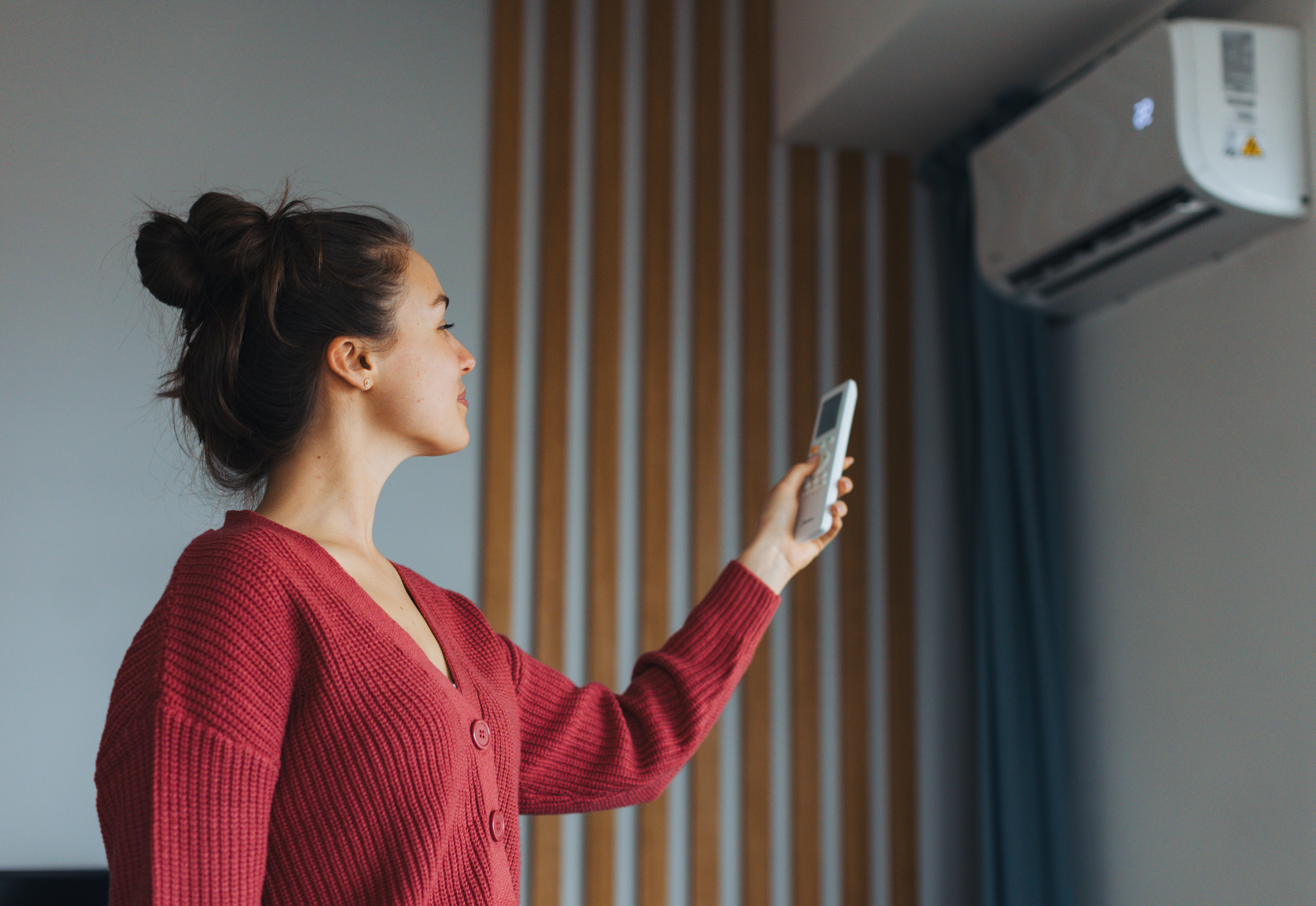 Woman adjusting air conditioning with remote control